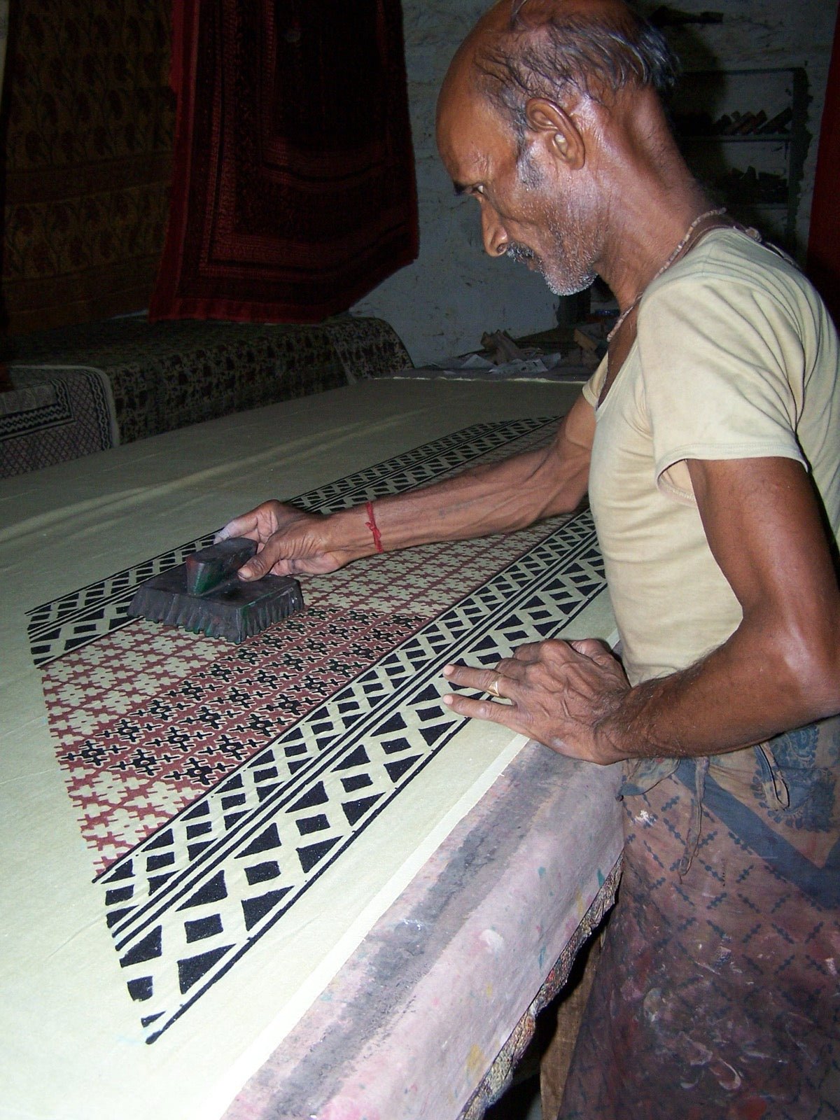 Artisan hand block printing cloth with carved wooden stamp and dye pad.